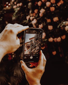 Hands holding smartphone to photograph floral-covered architecture in Stresa, Italy.