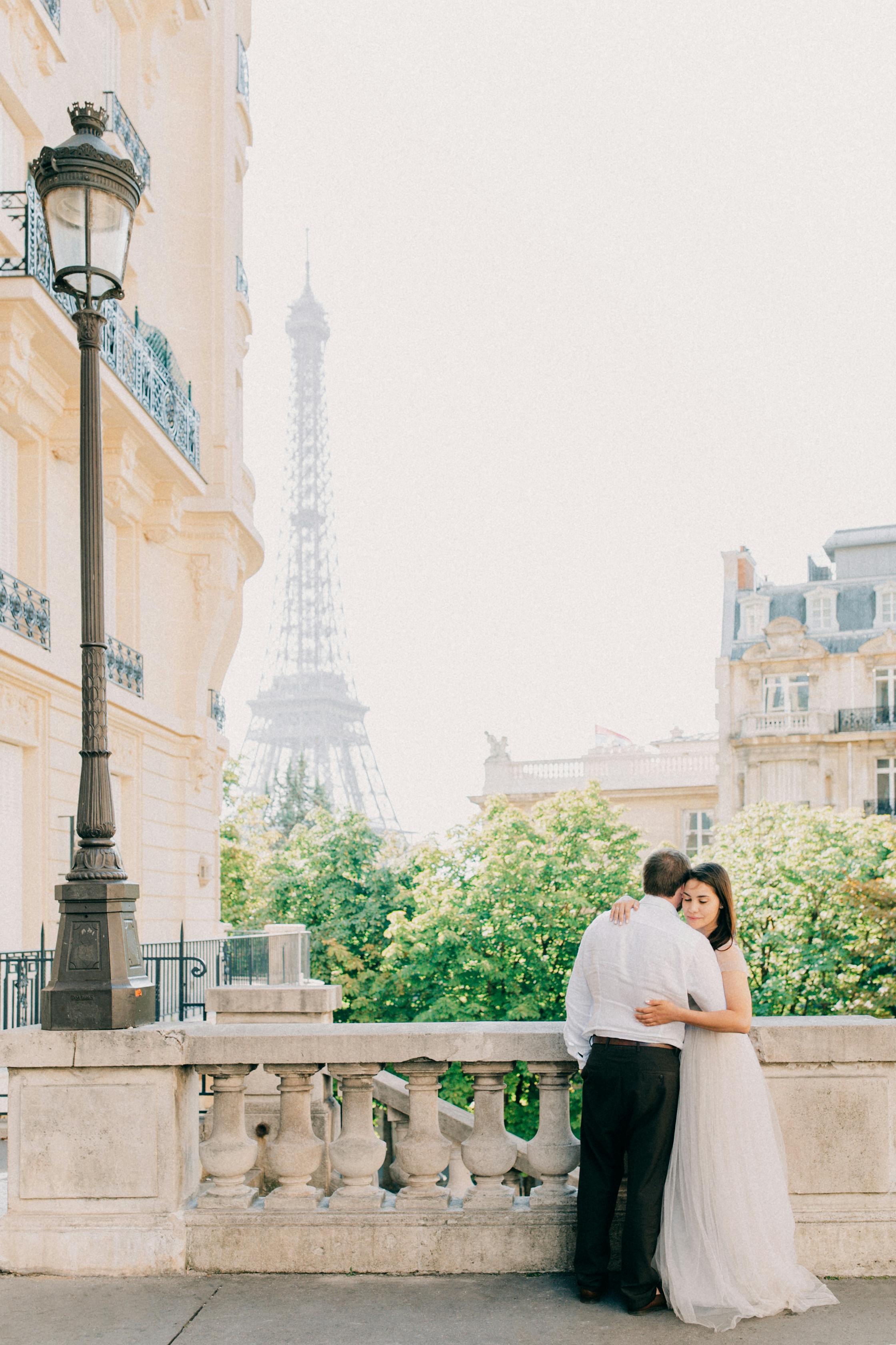 Couple embracing on a Parisian balcony with Eiffel Tower view, ideal for wedding imagery.