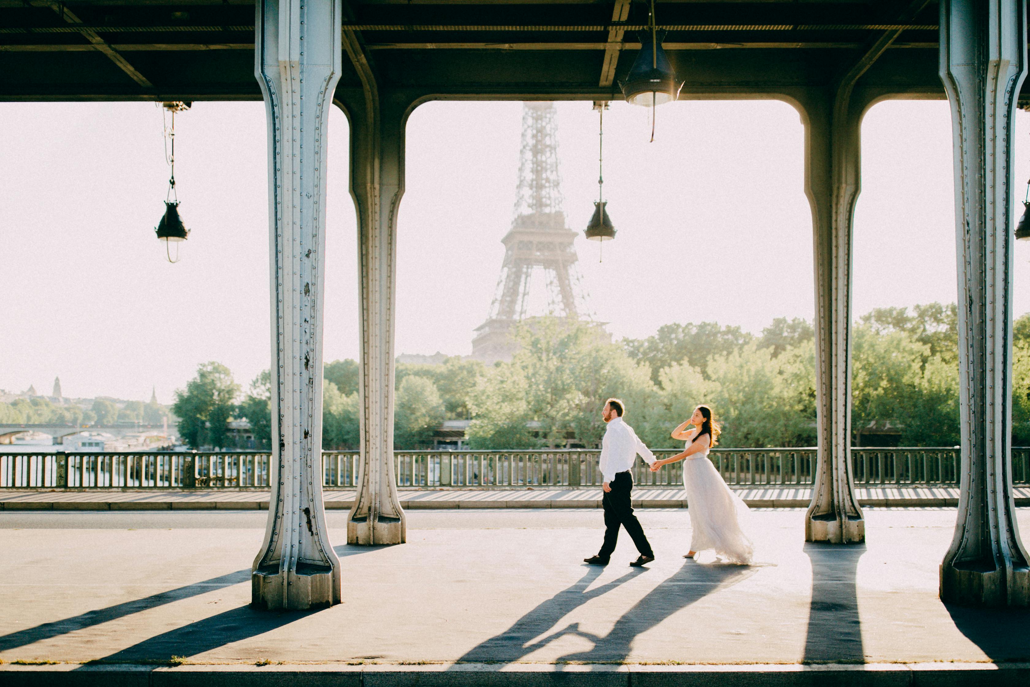 A couple strolling hand in hand under a Parisian bridge with Eiffel Tower view.
