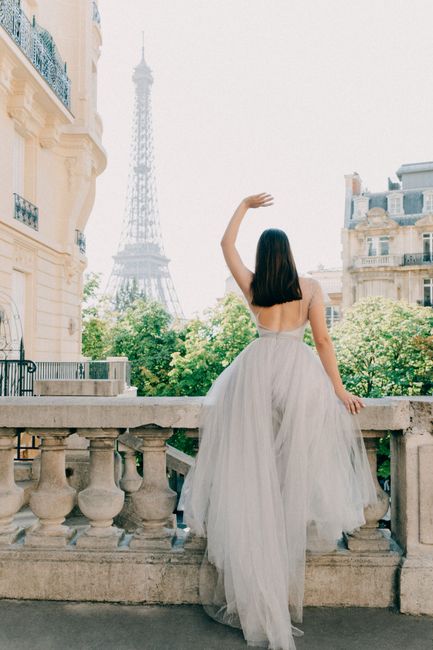 Woman in tulle dress gazing at Eiffel Tower from Parisian balcony.