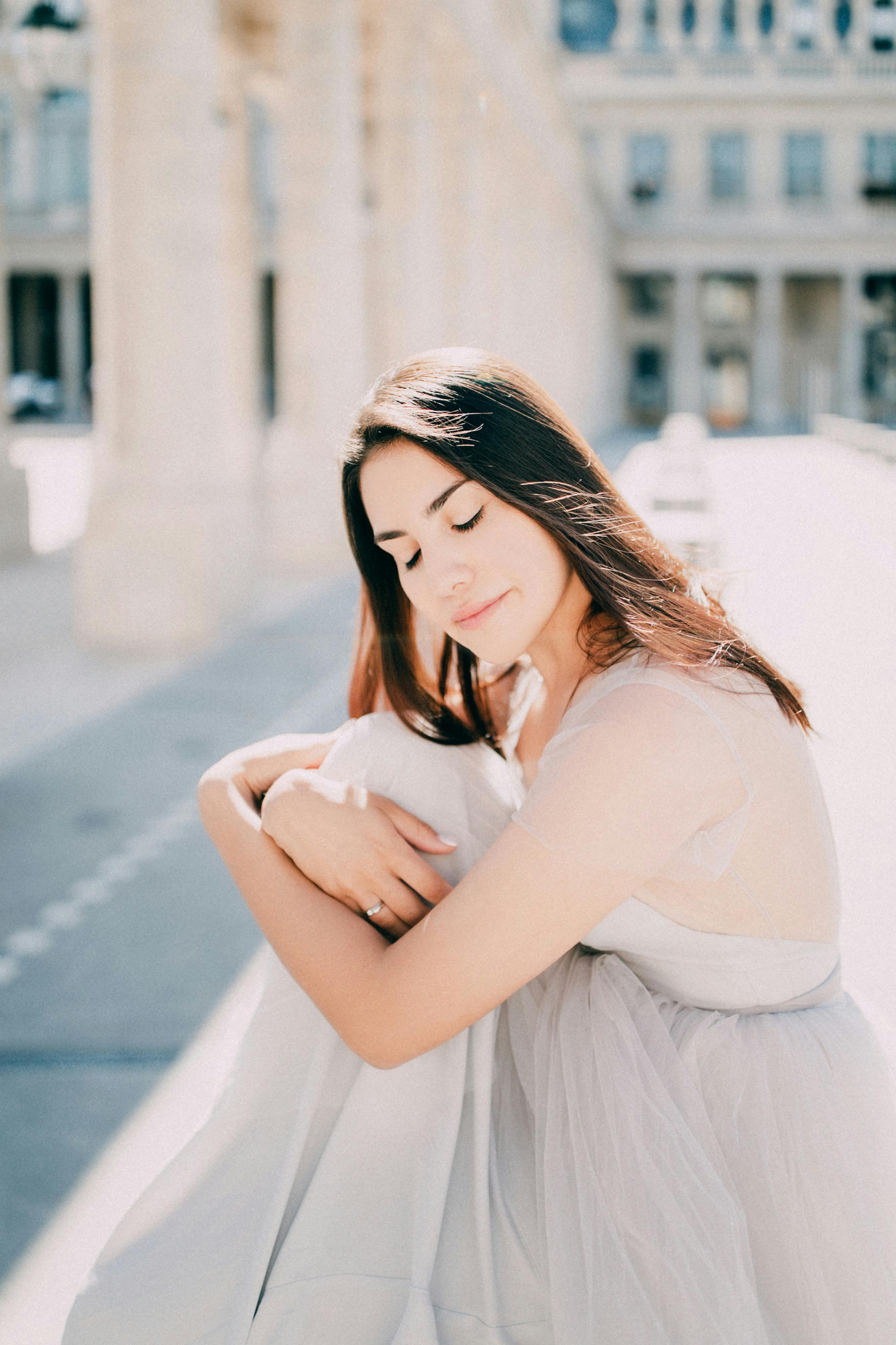 A serene bride in a light wedding dress embraces sunlight in an elegant outdoor location.