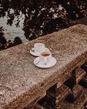 Two cappuccino cups on a stone terrace in Stresa, Italy, capturing a serene lake view.