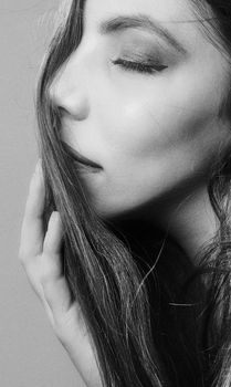 Close-up black and white portrait of a woman with eyes closed, touching hair.