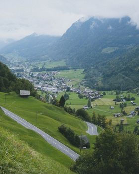A beautiful valley town surrounded by lush mountains and winding roads captured on a cloudy day.
