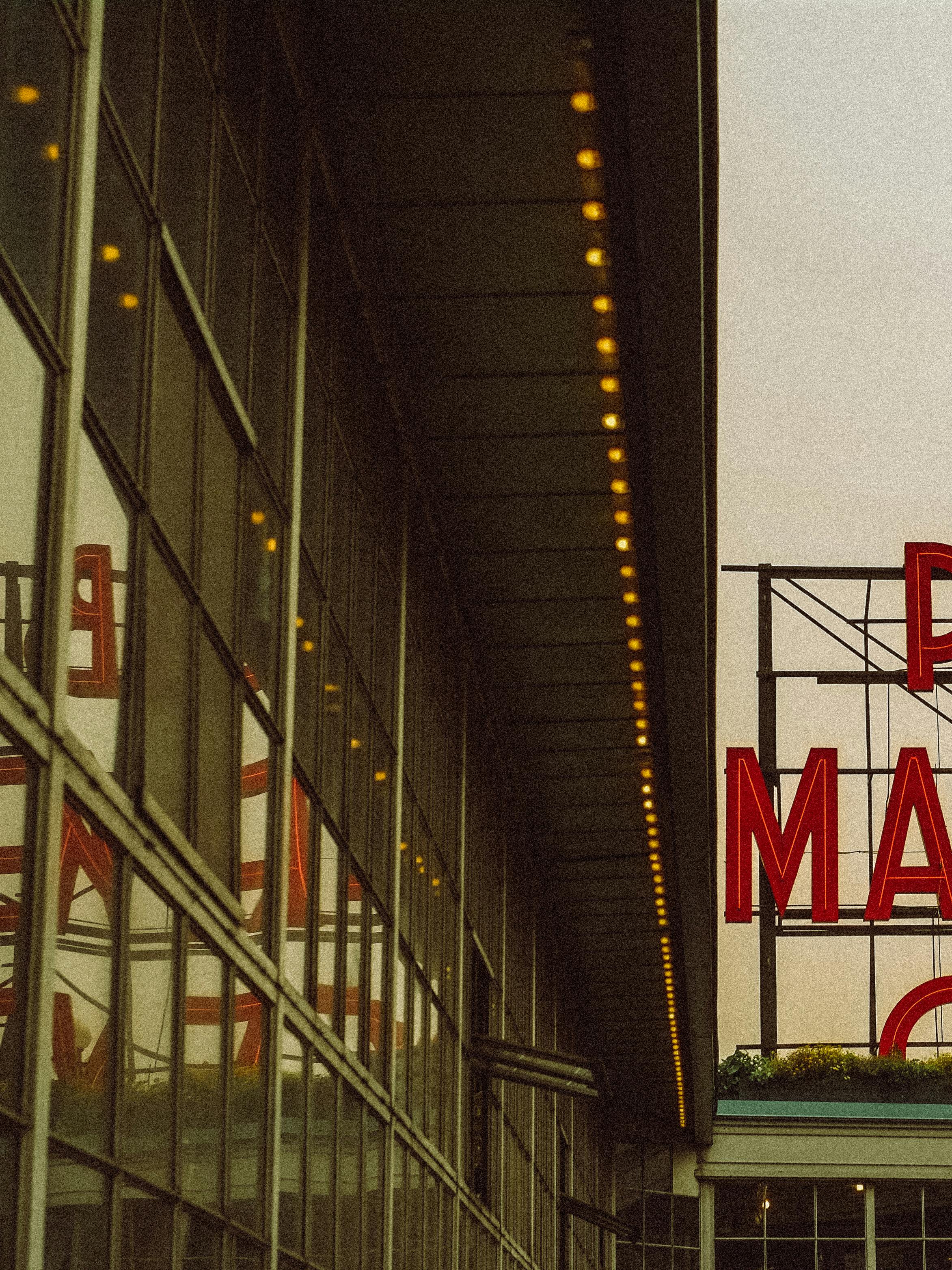 Urban market sign with neon lights reflecting on glass windows at dusk, creating a vibrant urban scene.
