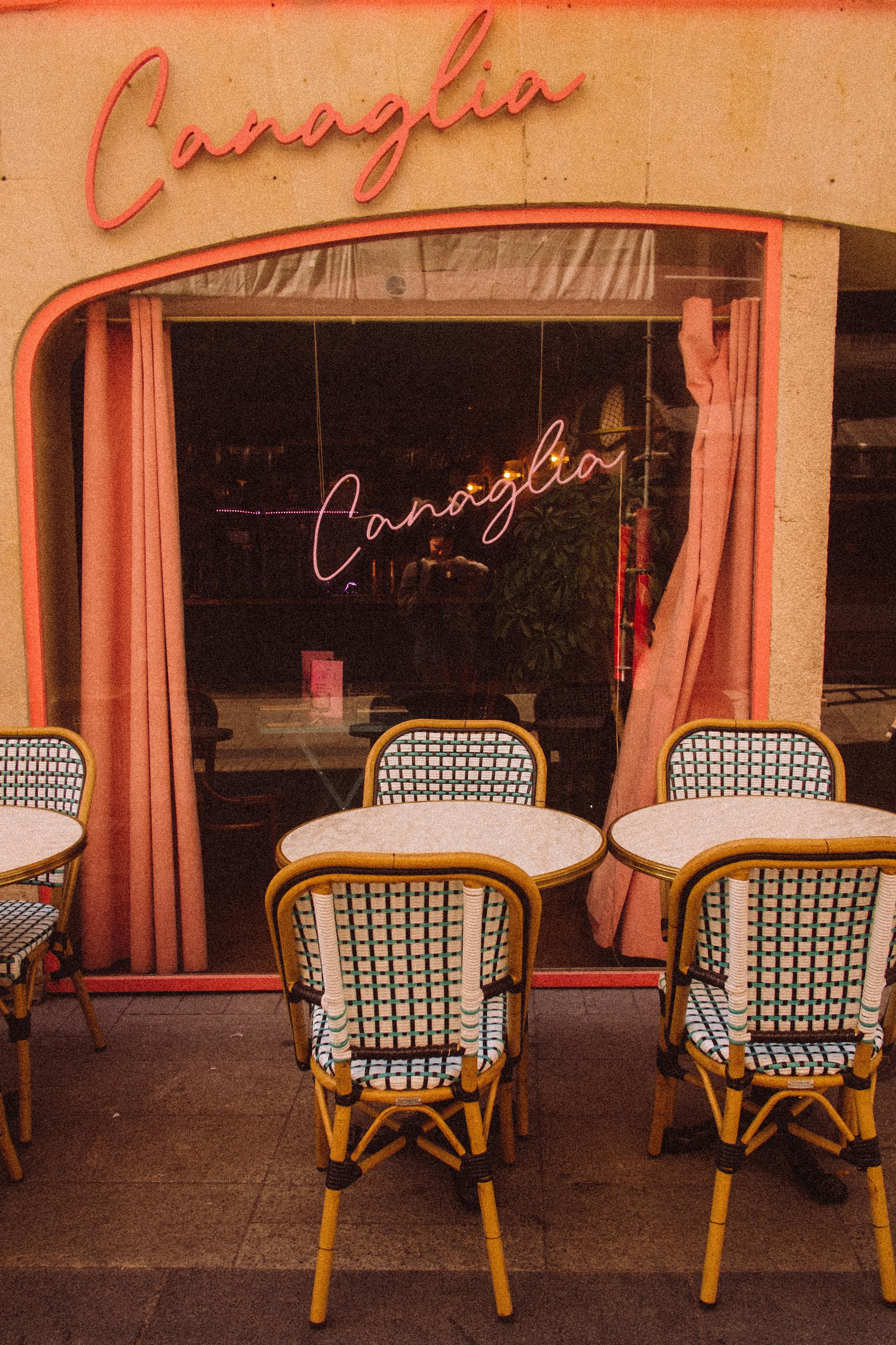 Outdoor café seating with elegant chairs and neon signage on a city street.
