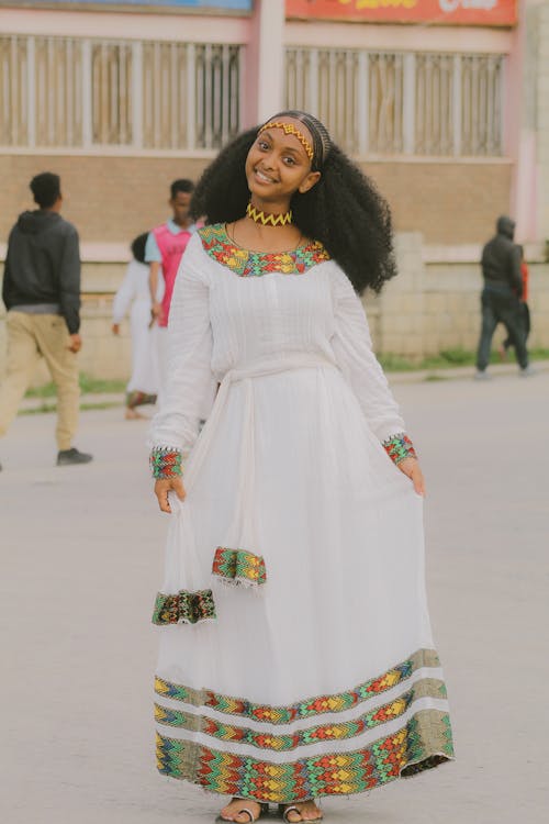 Young Woman in a Dress with Traditional Patterns Standing on the Street and Smiling 