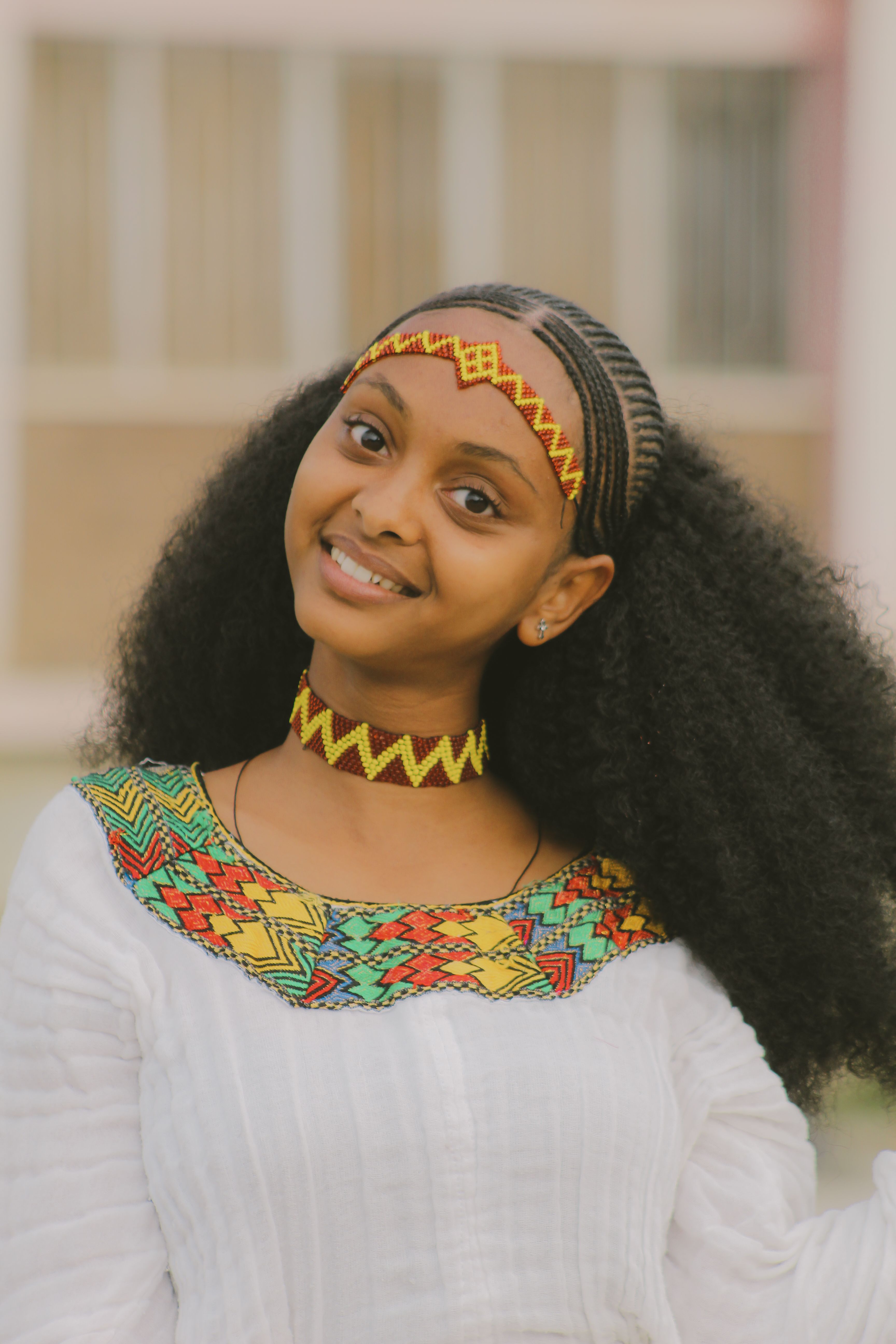 Portrait of a smiling woman in colorful traditional African clothing and accessories.