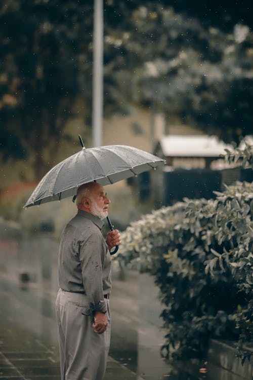 An Elderly Man with an Umbrella Standing on the Pavement 