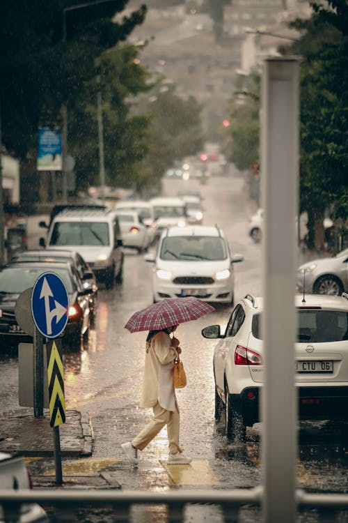 A Woman with an Umbrella Crossing a Busy Street in Heavy Rain 