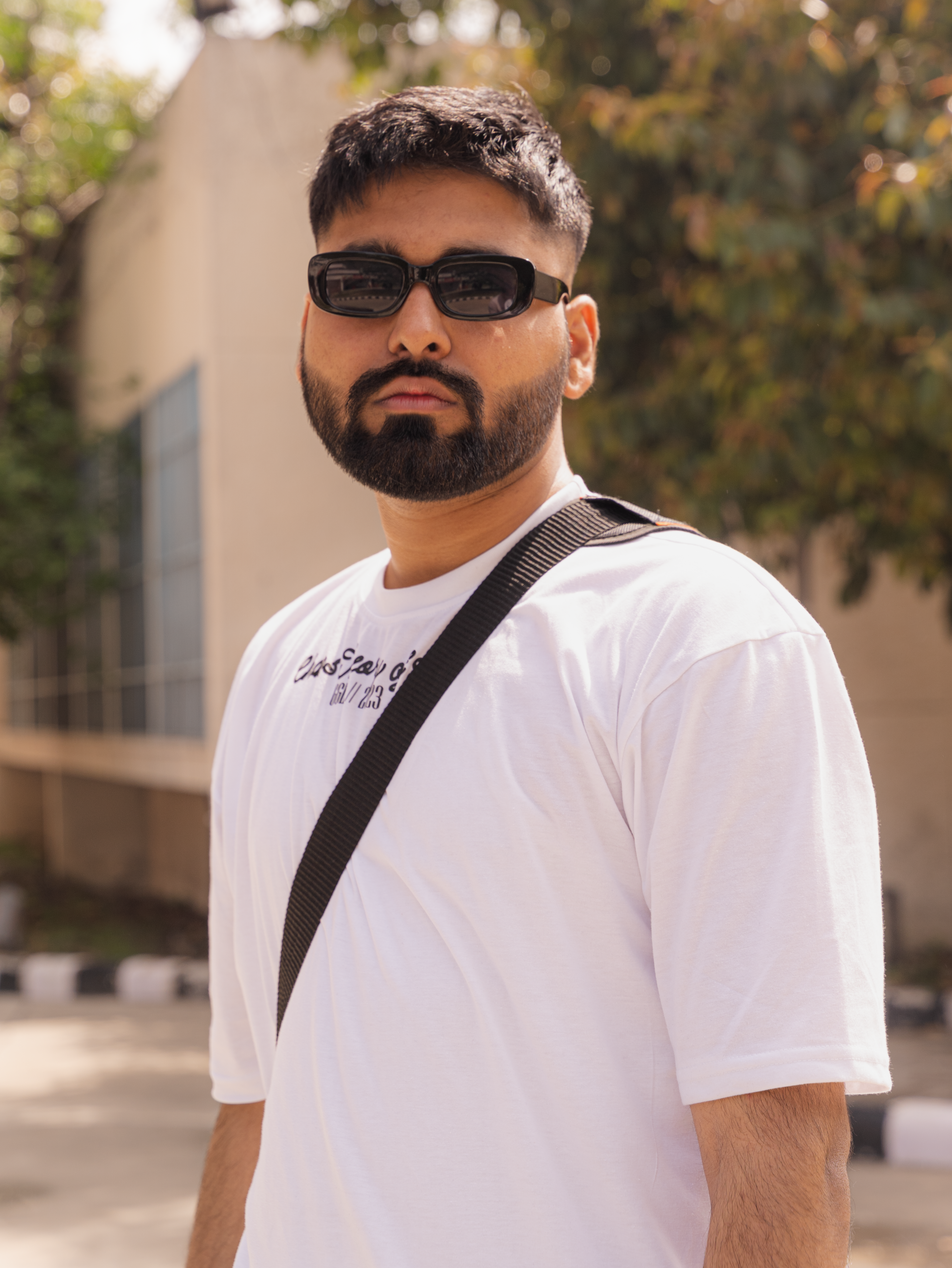Stylish bearded man in sunglasses and white t-shirt outdoors, showcasing a modern fashion look.