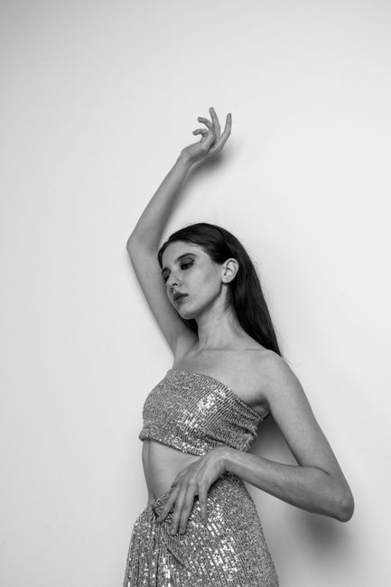 Black and white portrait of a woman elegantly posing in a sequined outfit in a studio setting.