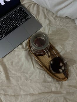A warm setup with coffee cups and a laptop on a bed, perfect for remote work.