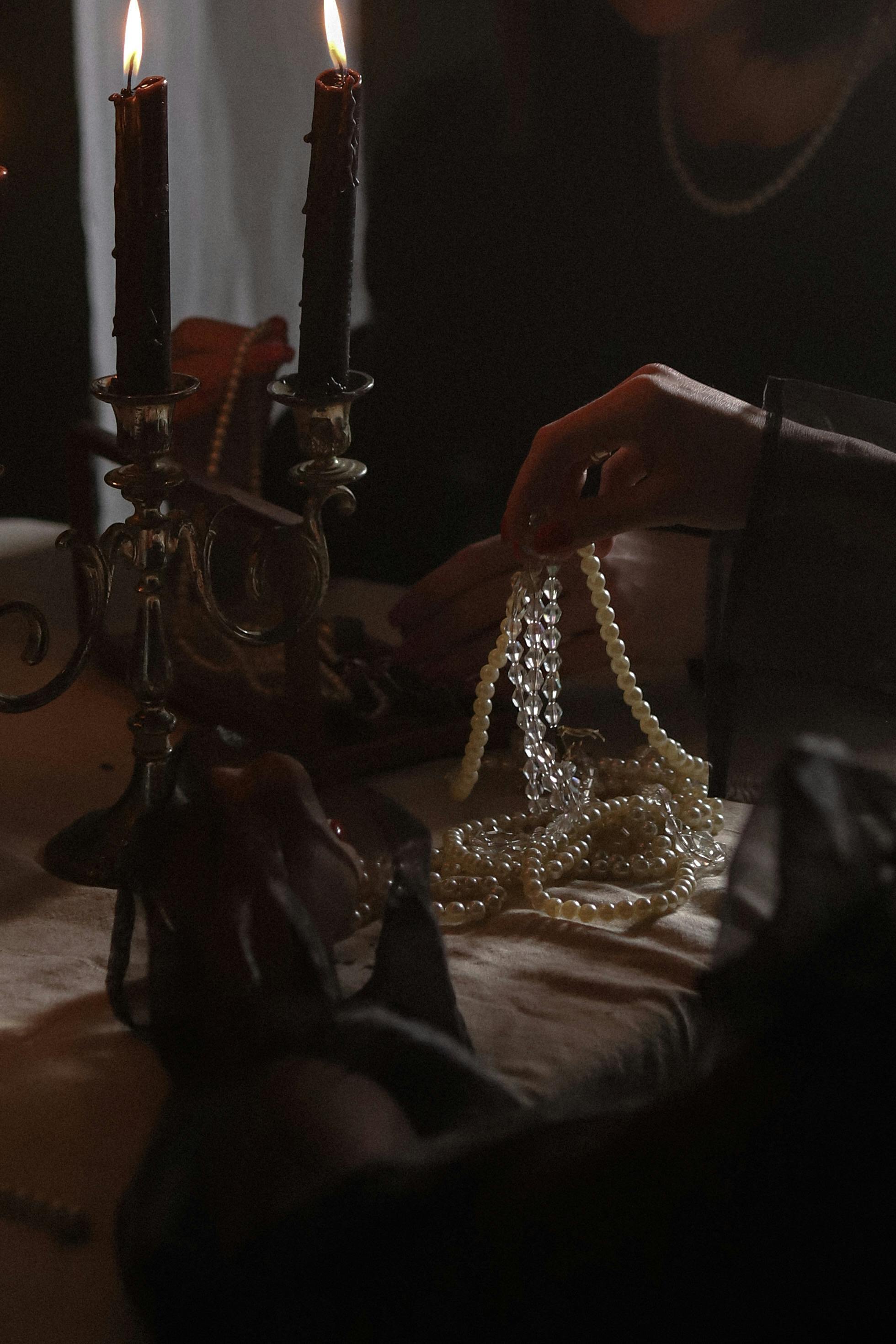 A moody, elegant scene of a woman handling pearls by candlelight, showcasing luxury and sophistication.