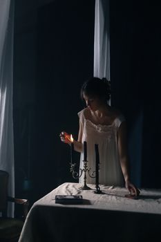 A woman in a nightgown lighting candles on a table, creating a retro and moody ambiance.