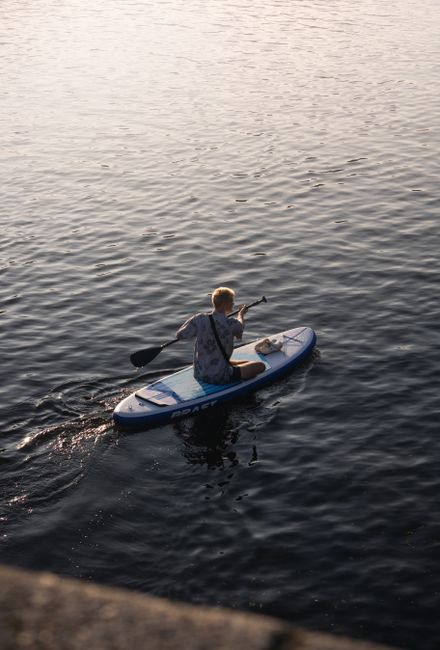 A person paddles leisurely on a calm lake during sunset, enjoying outdoor recreation.