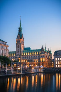 The illuminated Hamburg Townhall with reflections in the canal during a tranquil evening dusk.