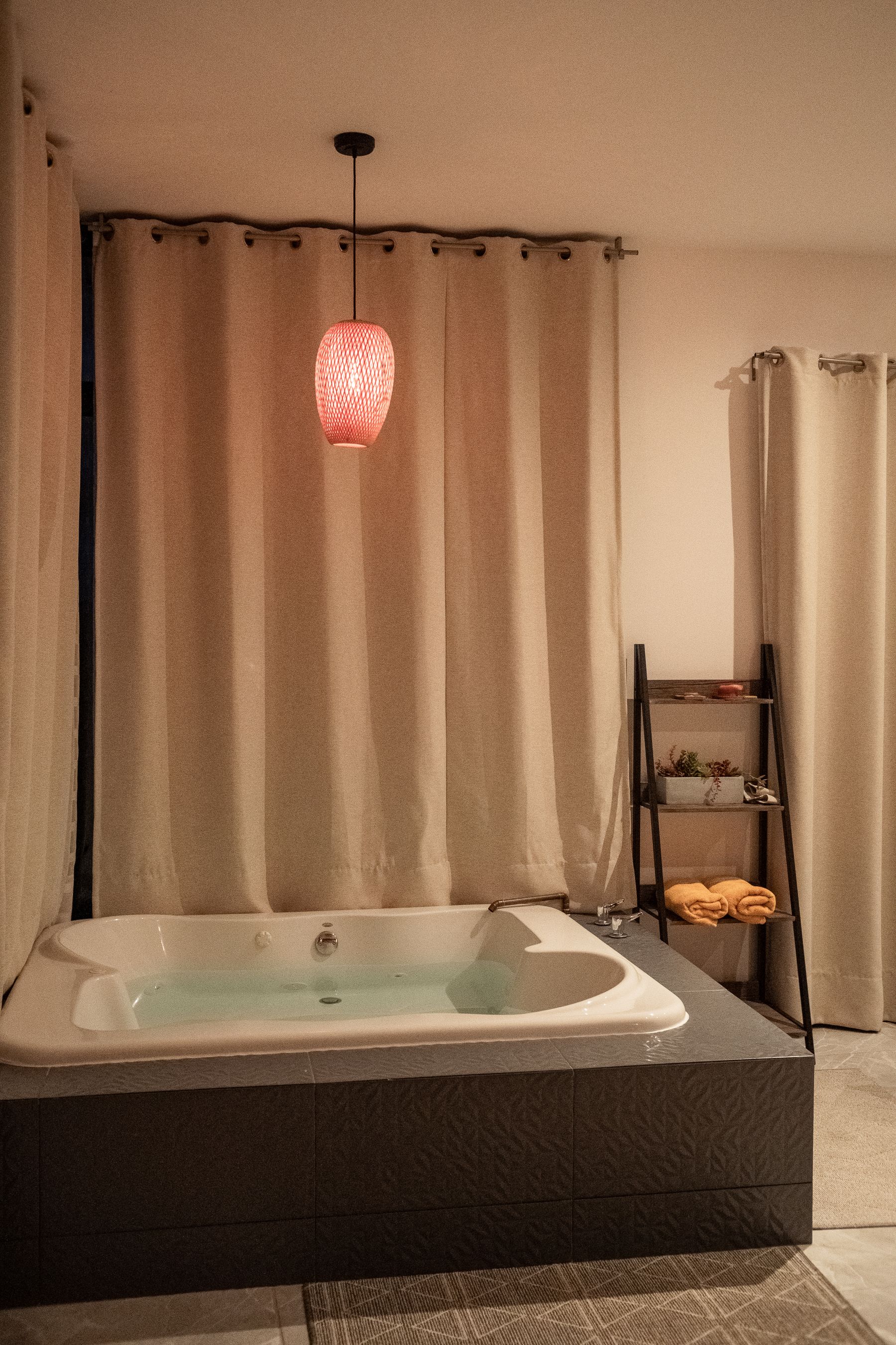 Cozy bathroom with a large rectangular bath, full-height soft curtains, warm pendant light and a towel ladder