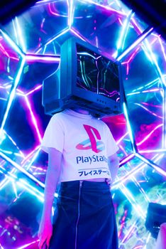 Person wearing retro TV as helmet surrounded by vibrant neon lights.