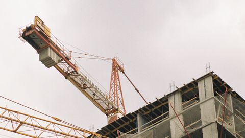 A high-rise building under construction with visible tower cranes and concrete structure.