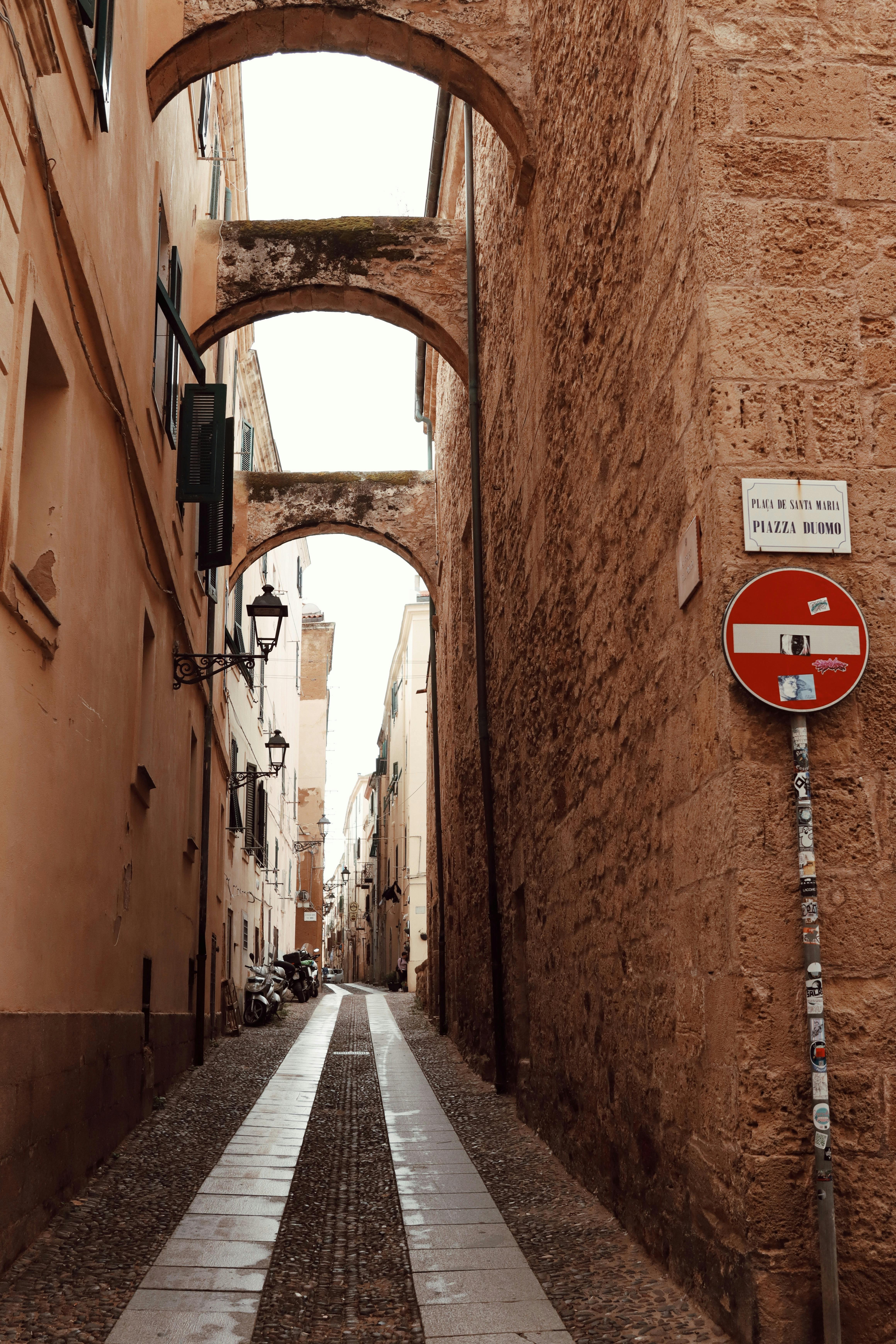 Explore the historic narrow streets of Alghero, Sardinia showcasing rustic stone arches and urban charm.