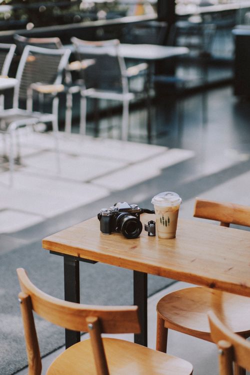 Free A digital camera and iced coffee on an outdoor cafe table in a modern setting. Stock Photo