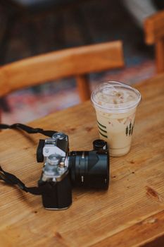 A vintage camera and iced coffee cup sit on a rustic wooden table indoors.