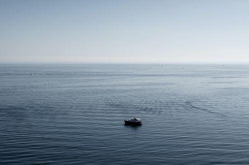 Free A lone motorboat floats on a calm, vast sea under a clear sky, ideal for travel and adventure themes. Stock Photo