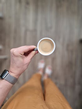A person's hand holding an espresso cup, view from above in an indoor setting.