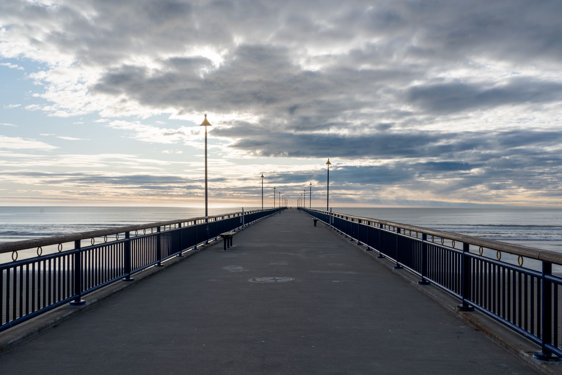 A serene view of New Brighton Pier in Christchurch, New Zealand during sunset, showcasing the expansive horizon and calm sea.