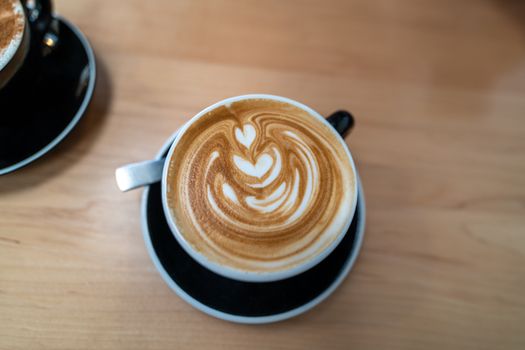 Delicious coffee with intricate latte art served in a black cup on a wooden table.