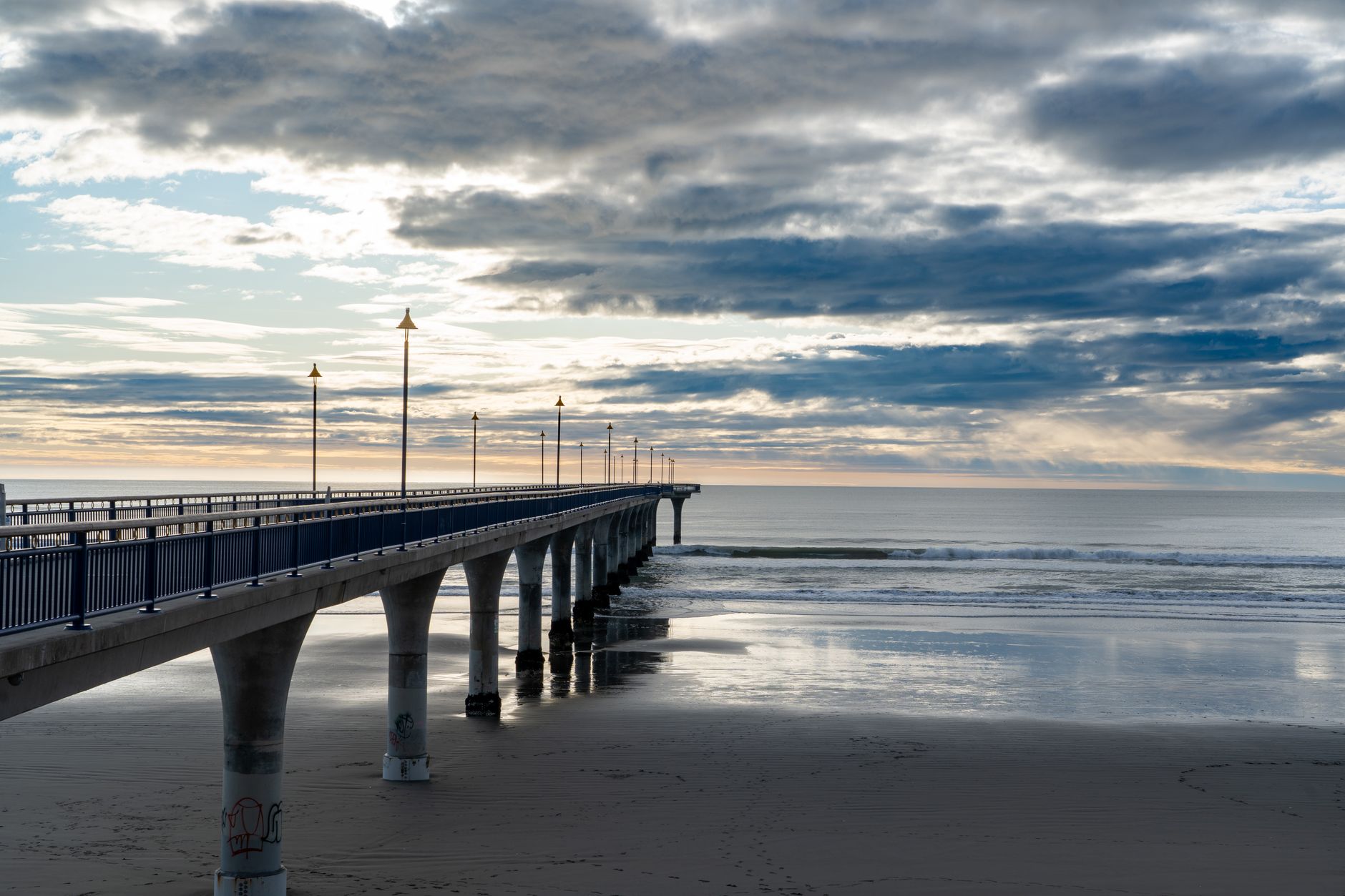 Serene view of New Brighton Pier stretching into the sea at sunset in Christchurch, New Zealand.
