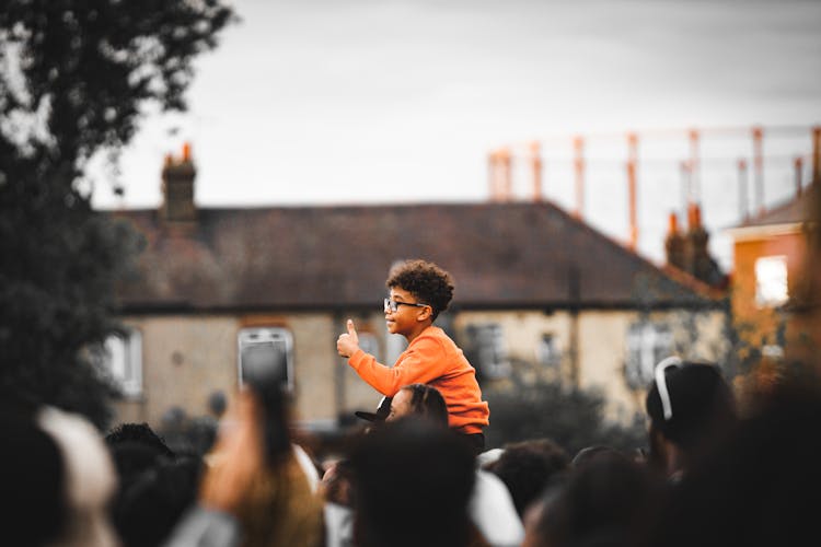 Curly Boy In Orange Sweatshirt And Eyeglasses Sitting On Fathers Shoulders