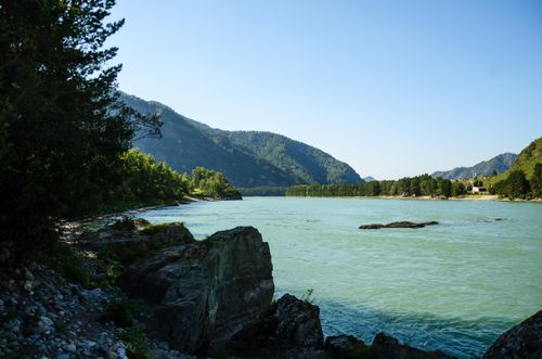 Free Tranquil river scene surrounded by lush hills and serene mountains. Stock Photo
