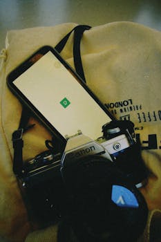 Vintage camera and smartphone placed on a London-themed bag, showcasing nostalgia in modern technology.
