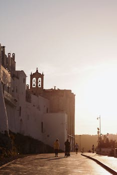 People stroll past a historic church during a golden sunset, creating a serene cityscape.