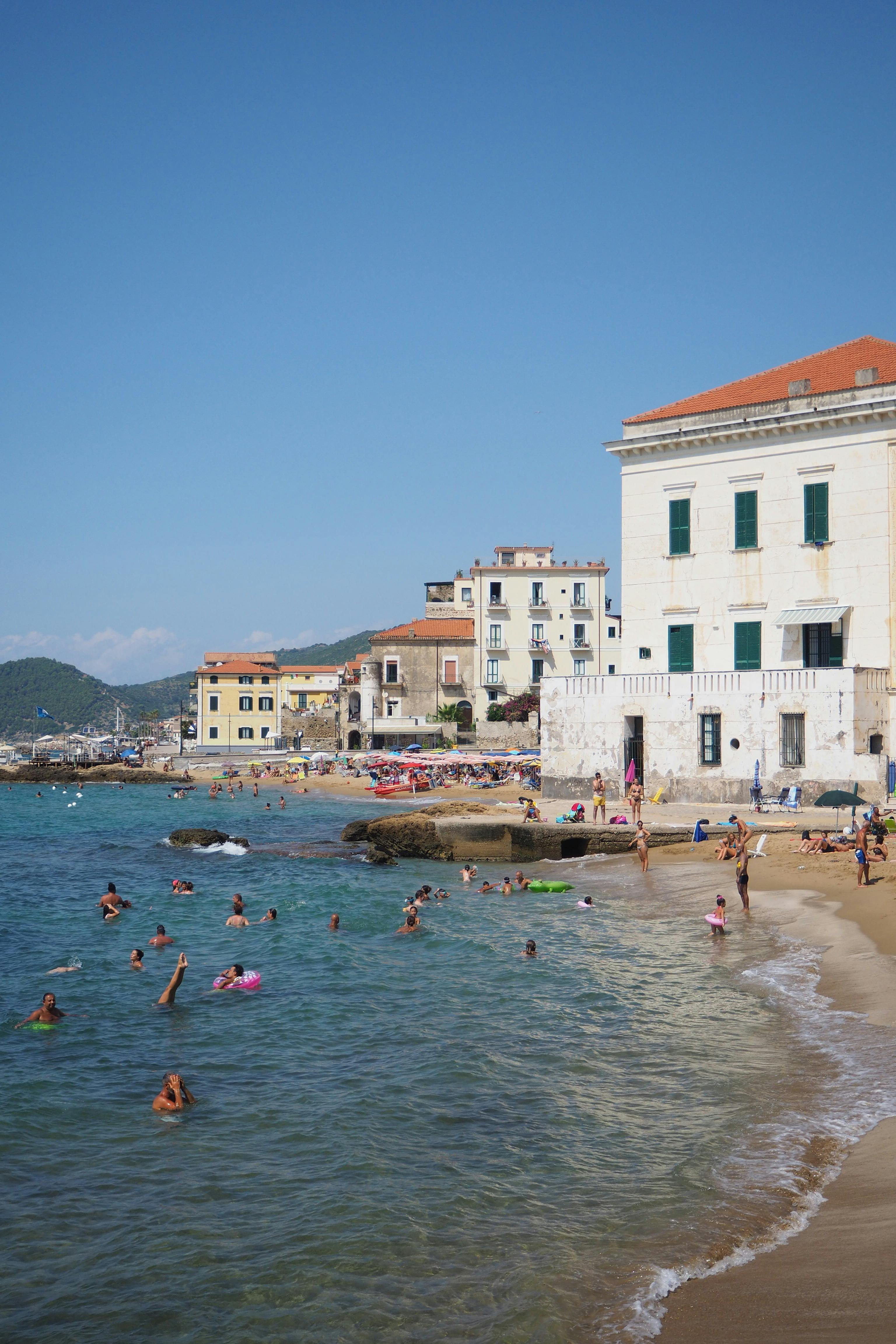 A lively beach scene in a Mediterranean town with people enjoying the summer by the sea.