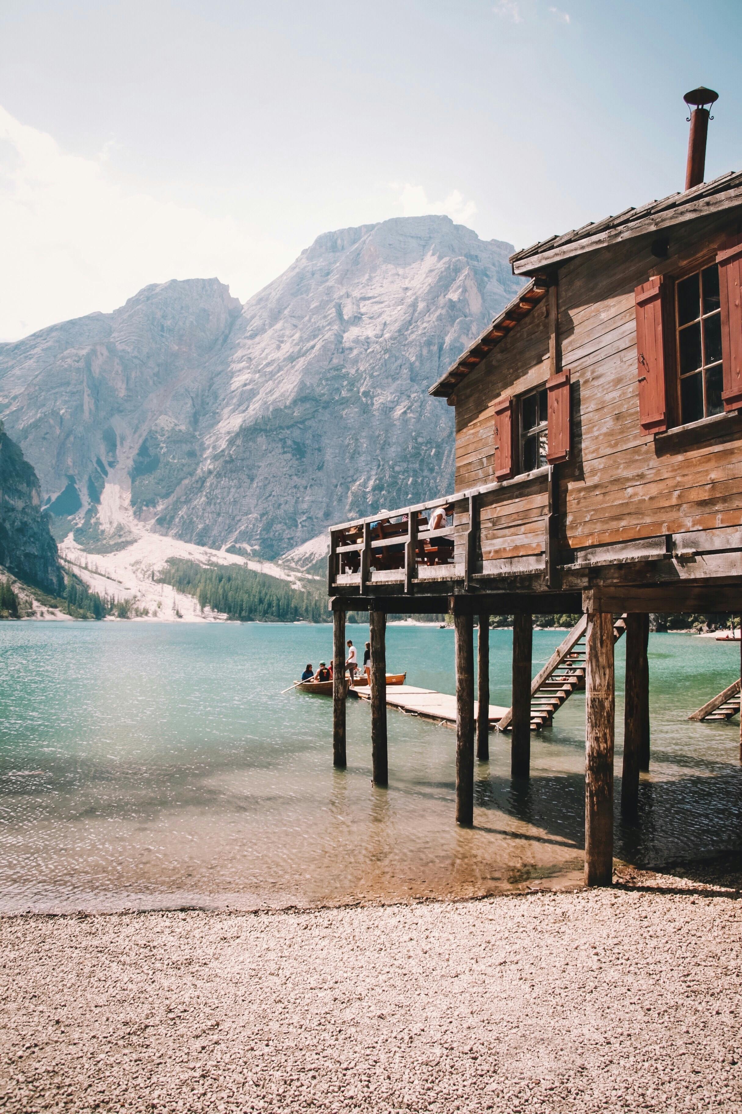Rustic wooden cabin by a tranquil lake against a mountain backdrop, capturing serene beauty.