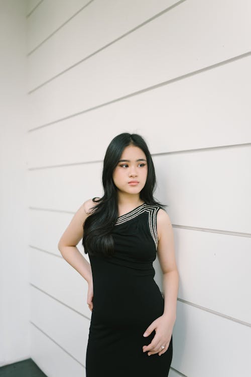 Young Woman in a Black Dress Posing against a White Wall 