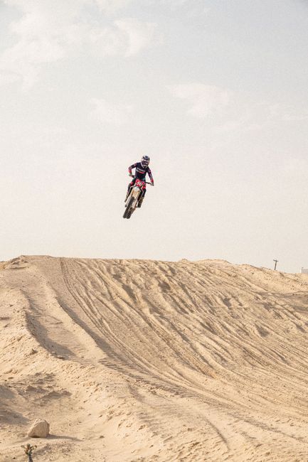 Motocross rider jumps high above desert dunes capturing the adrenaline of the sport.