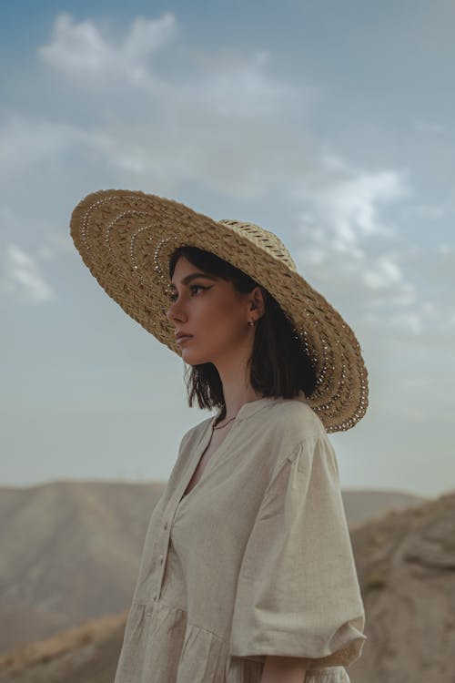 Young Woman in a Dress and Hat Posing Outside 