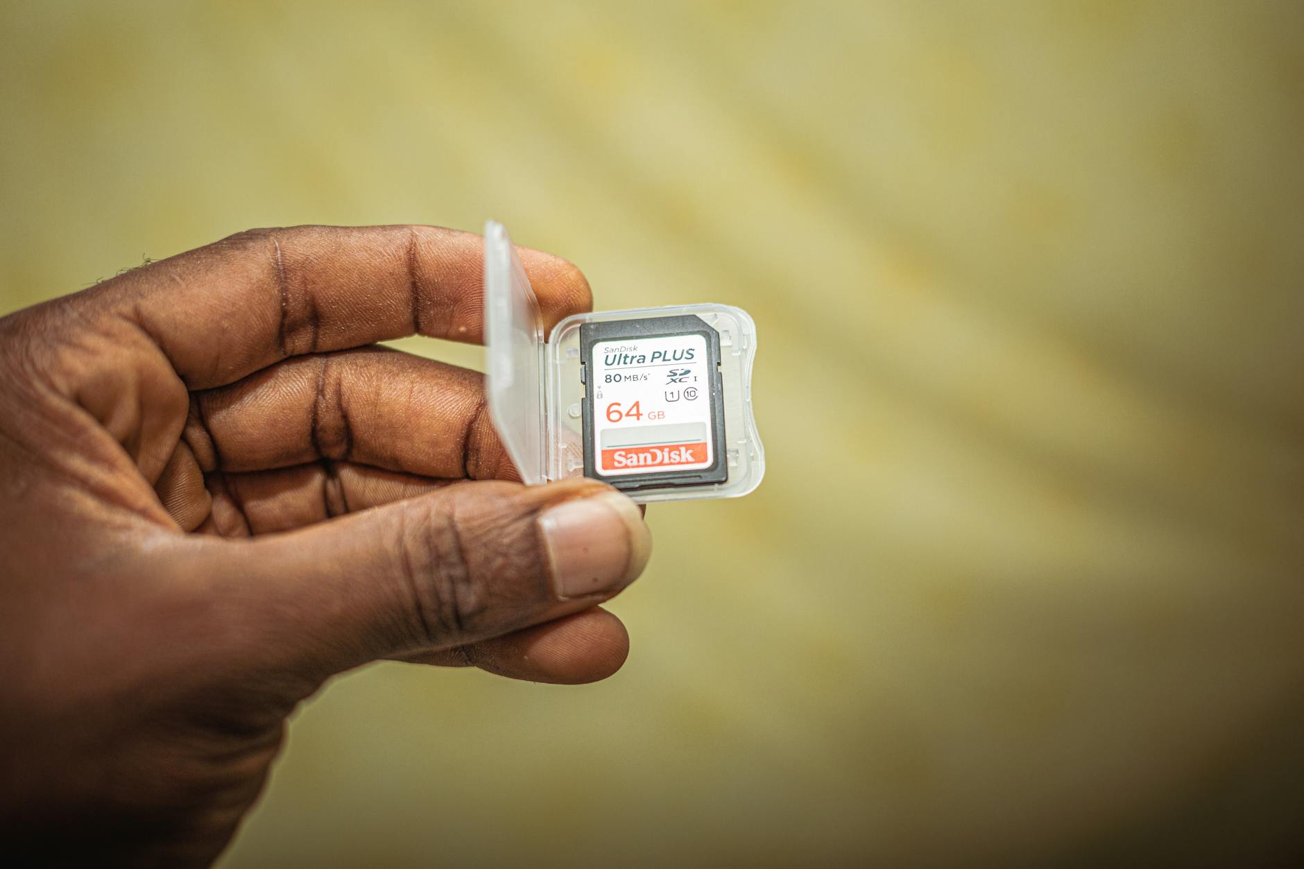 A close-up view of a hand holding a 64GB SanDisk memory card in a plastic case.