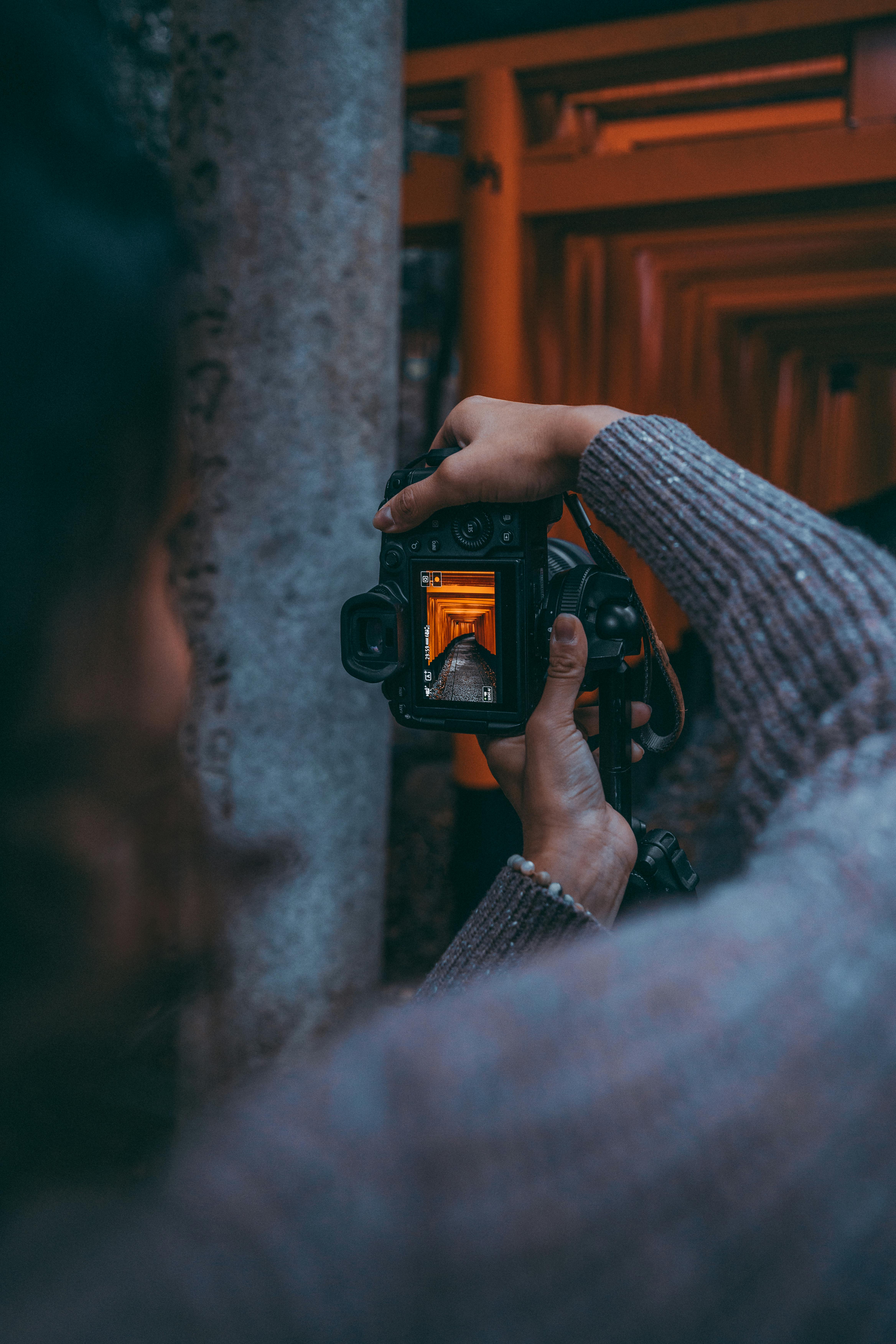 A photographer captures Kyoto's iconic Fushimi Inari Taisha torii gates through a camera's viewfinder.