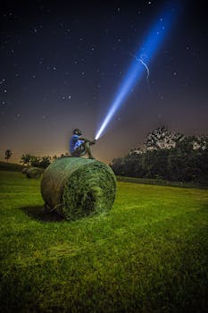 一名男子坐在田野的干草捆上，用手电筒照亮繁星点点的夜空