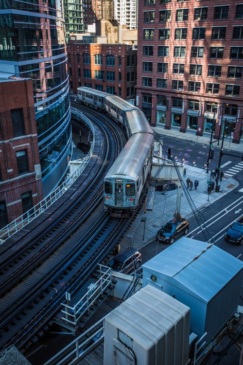 Free A city train travels on elevated tracks curving through modern skyscrapers. Stock Photo