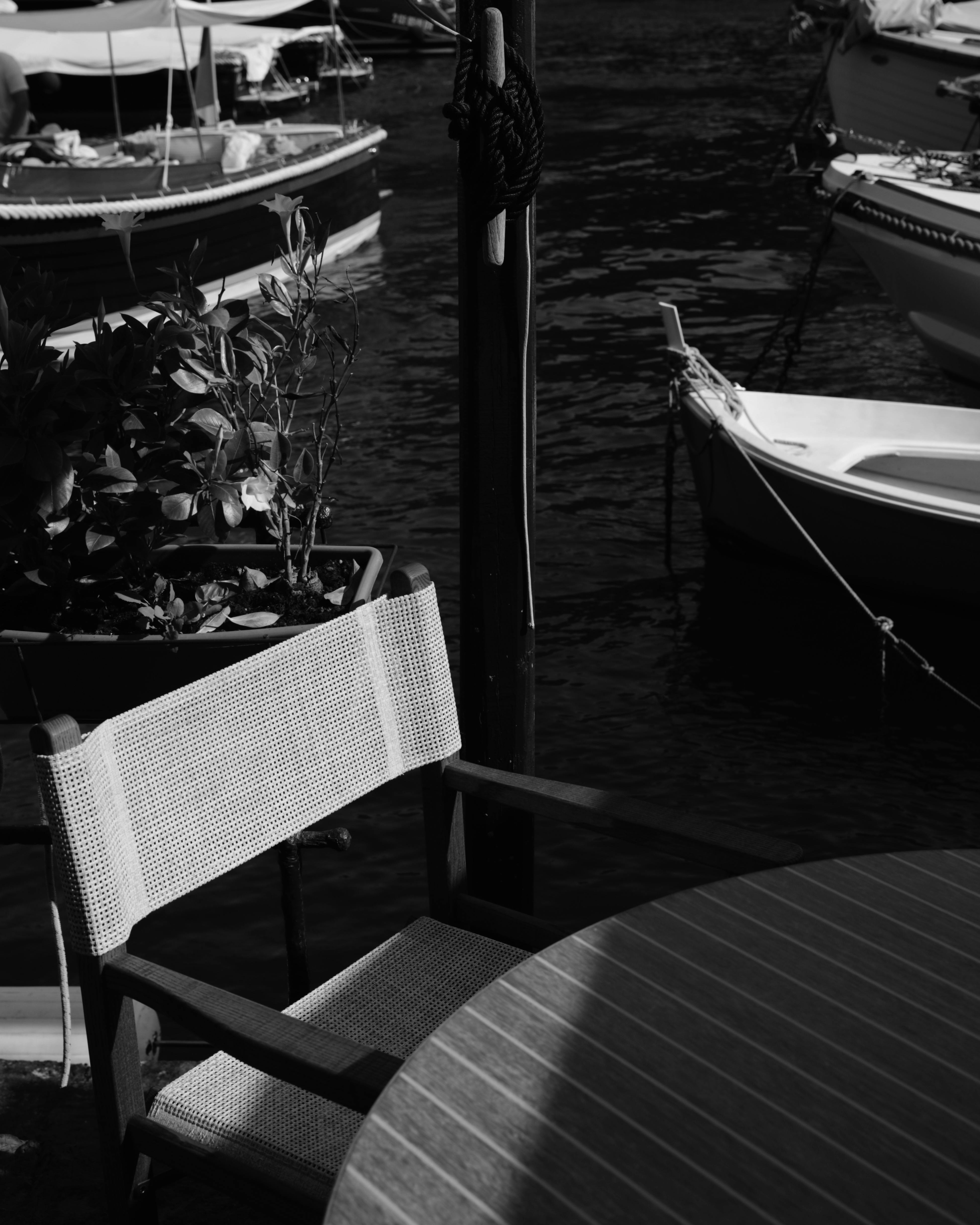 Black and white photo of a marina in Portofino, Italy, featuring boats and outdoor seating.