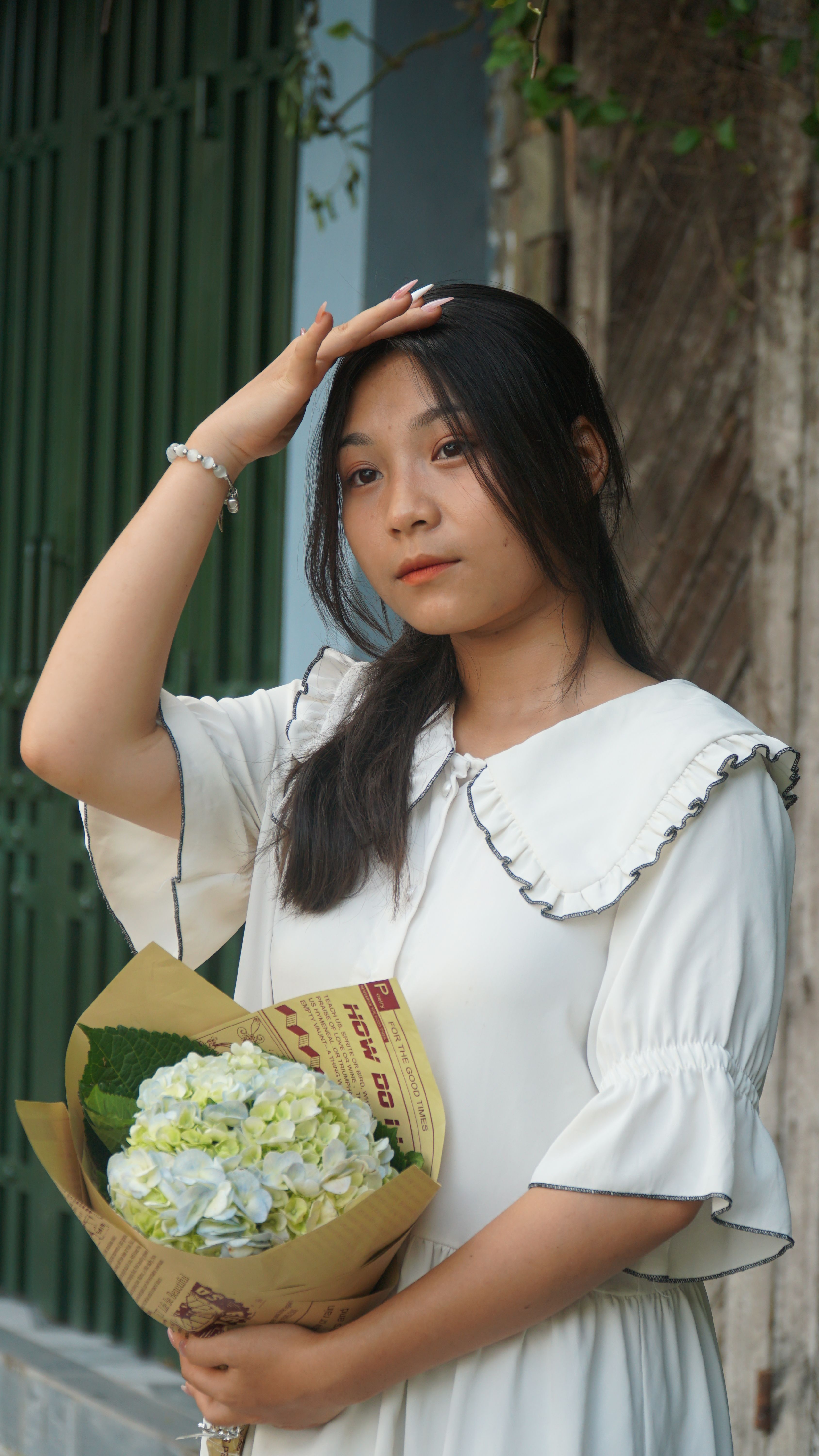 Charming portrait of a woman in white dress holding a bouquet of flowers outdoors.