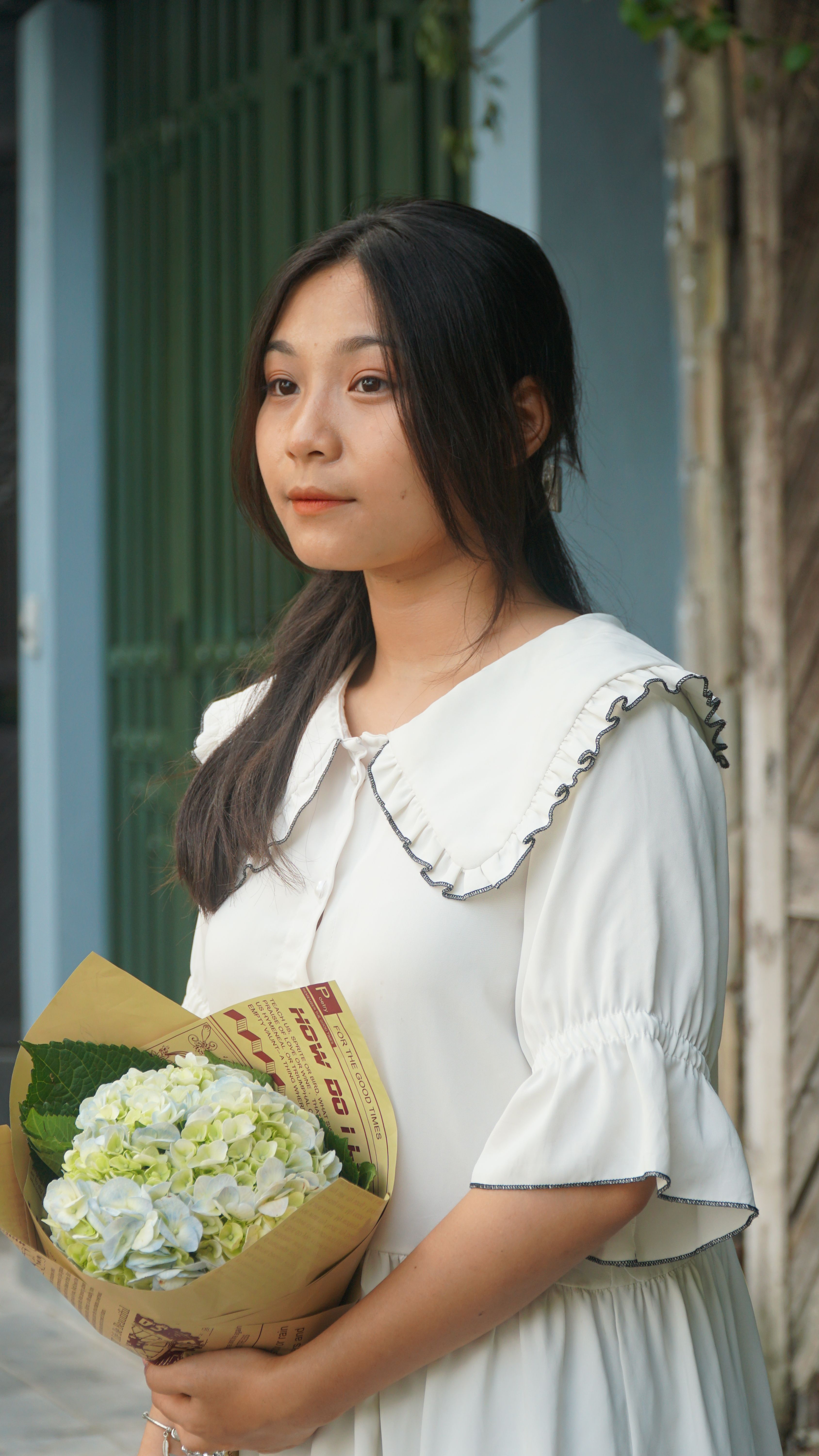 A serene portrait of an Asian woman holding a bouquet of flowers, outdoors.