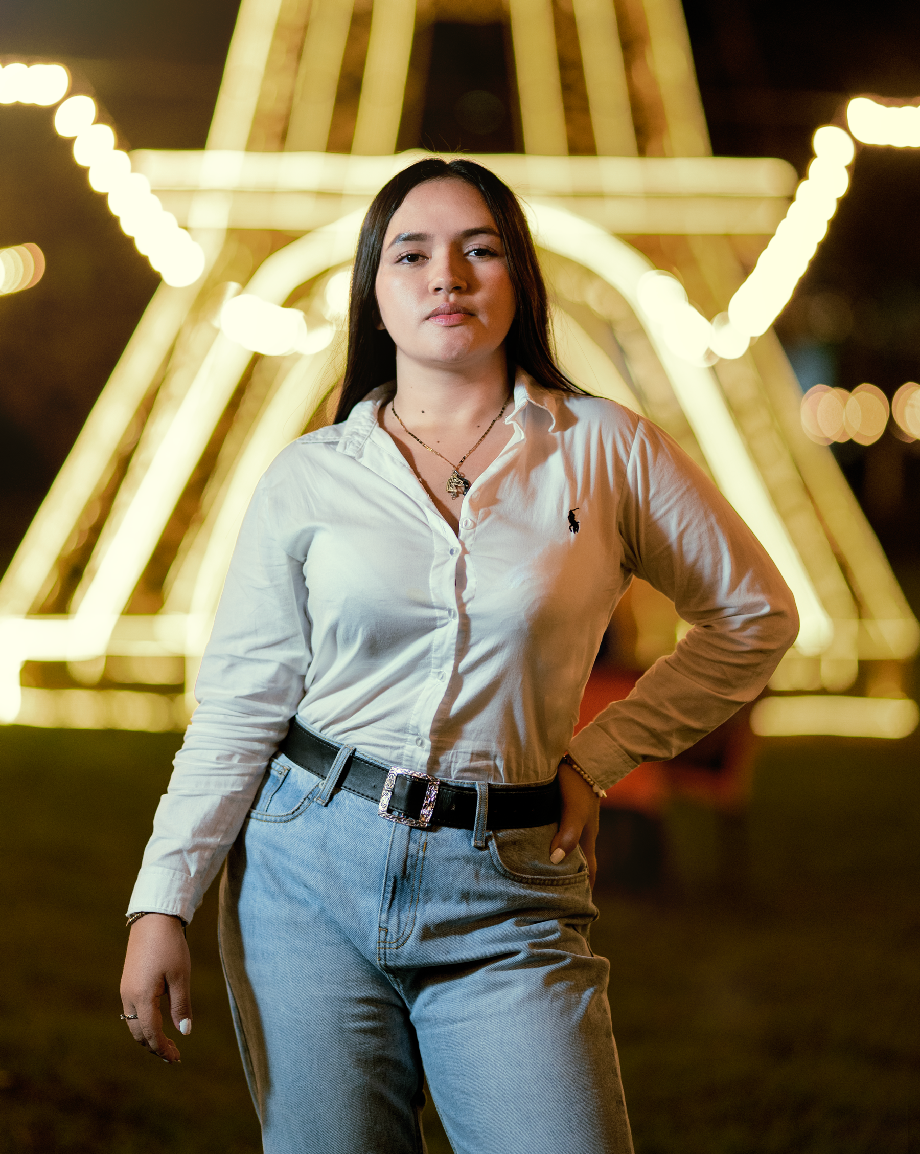 Portrait of a confident woman in a white shirt with light installation in the background at night.
