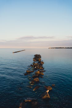 Peaceful ocean scene with a row of rocks and distant horizon during sunset, perfect for travel inspiration.